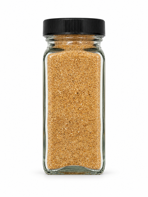 A clear glass spice jar filled with a golden-brown granular seasoning blend, sealed with a black ribbed screw-top lid, isolated on a white background.