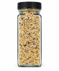 A clear glass spice jar filled with a coarse yellow and beige seasoning blend, topped with a black ribbed screw cap, isolated on a white background.
