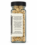 A clear glass spice bottle filled with a beige and brown seasoning blend, featuring a black ribbed cap and a cream-colored label with black text.